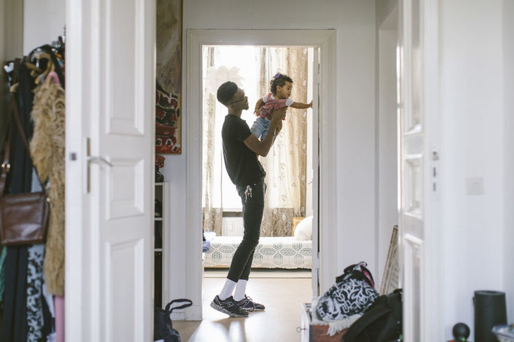 Side view of young man lifting daughter while standing at doorway in house