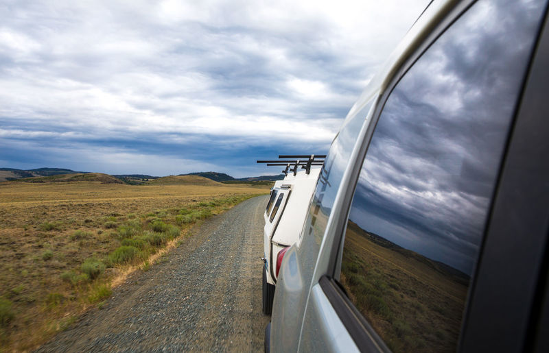 Road amidst field against sky seen through car window