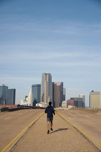 Back view of anonymous male gymnast in casual hoodie running with blue sky above downtown in dallas, texas