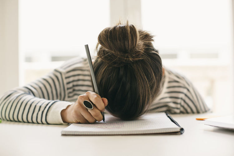 Woman writing on notepad resting her head on table