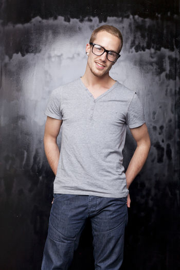 Portrait of young man wearing eyeglasses standing against old wall