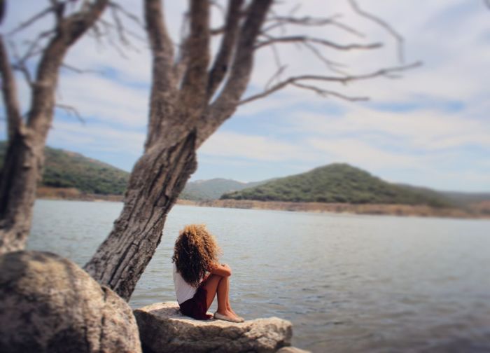 Side view full length of woman sitting on rock against lake