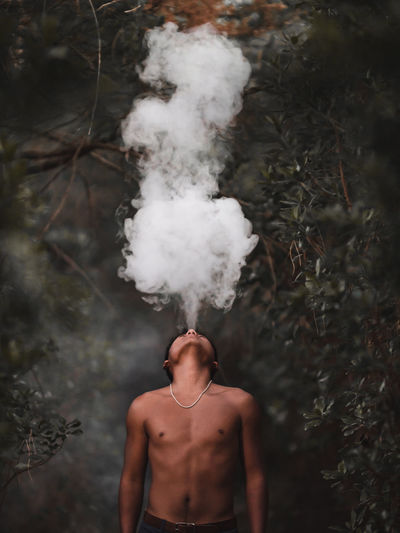 Shirtless man smoking while standing in forest