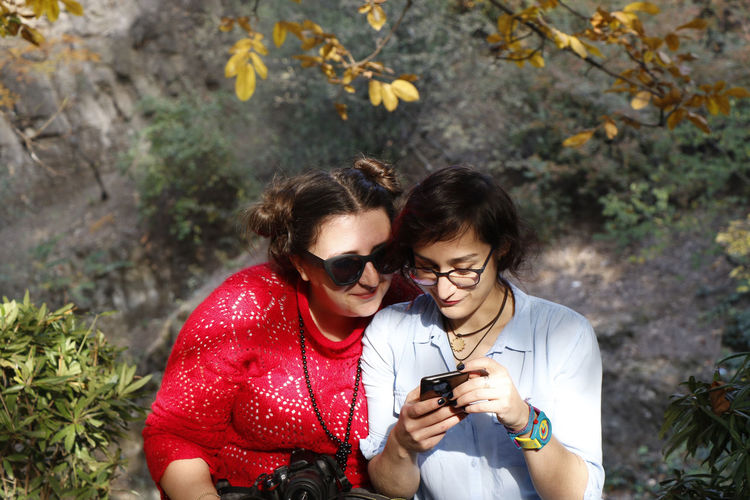 Two young woman looking to mobile phone, sunlight and smiling people.