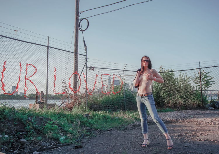 Full length portrait of woman standing by fence against sky