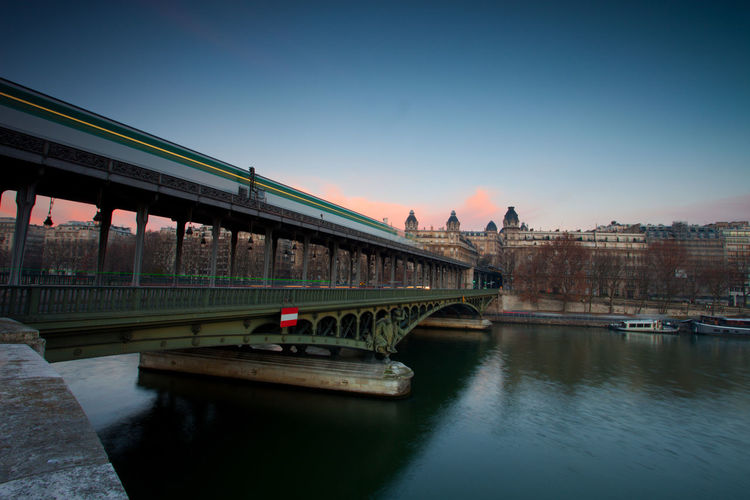 Bridge over river in city against sky during sunset