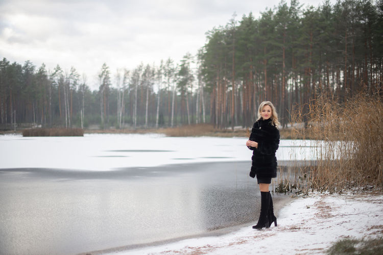 Full length portrait of woman standing by lake against sky during winter