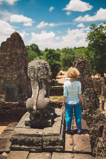 Rear view of woman standing by old statue at temple against sky