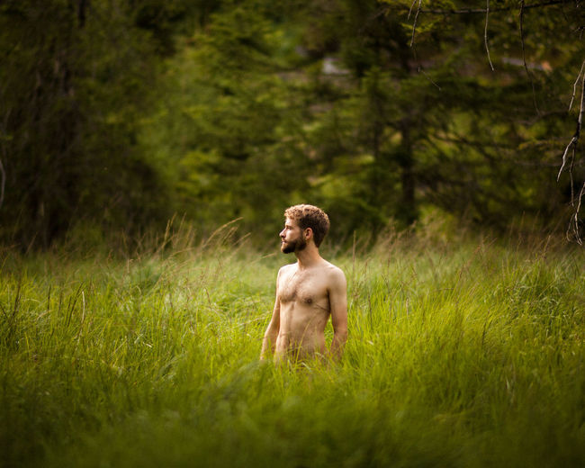 Shirtless young man standing on grassy land