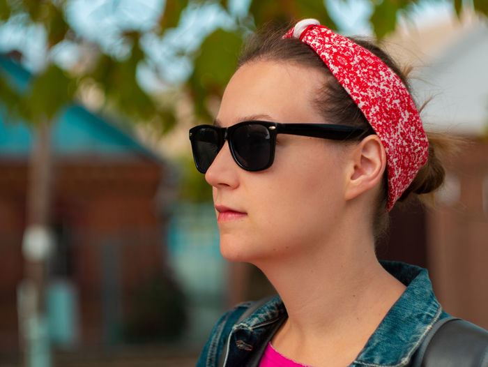 Pretty hipster woman in sunglasses, pink shirt, red bandana and denim jacket on sunny autumn nature.