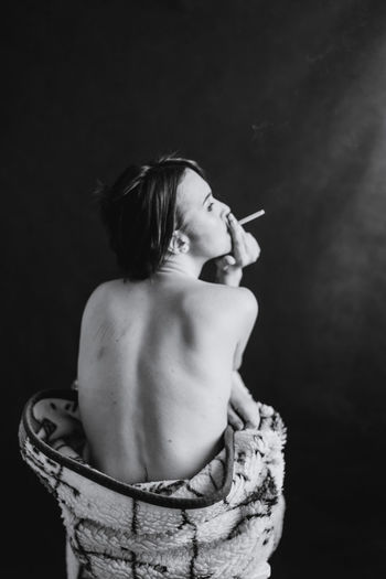 Rear view of shirtless woman smoking against wall