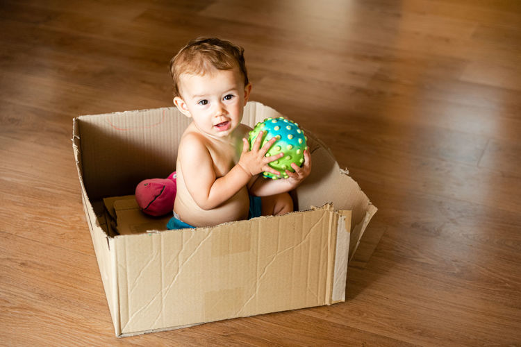 Portrait of baby boy sitting in box on hardwood floor