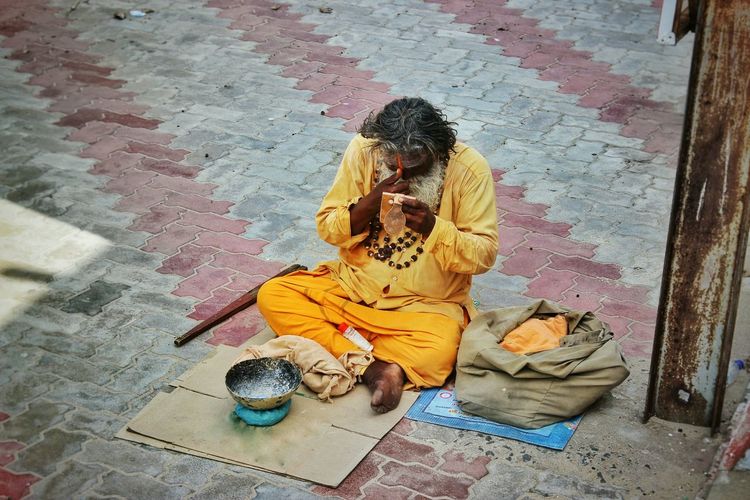 High angle view of sadhu sitting on cardboard at paved walkway