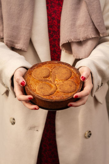 Unrecognizable female in elegant coat carrying delicious pie and showing dessert to camera