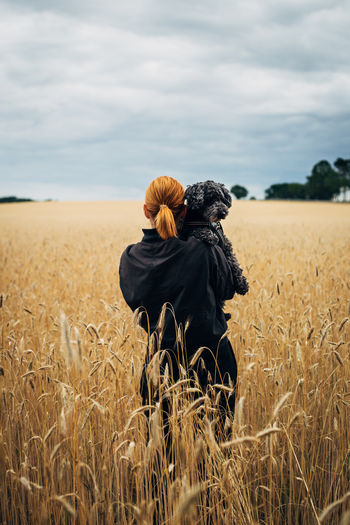Rear view of woman with dog standing in farm