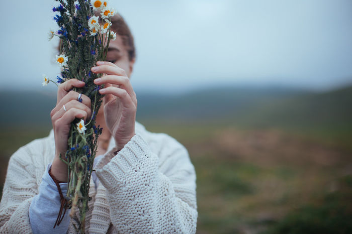 Close-up of woman holding flower on field against sky