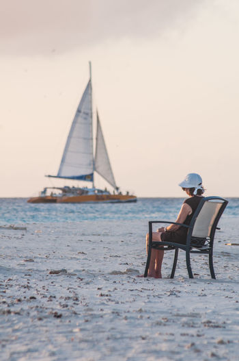 Woman sitting on chair by sea against sky