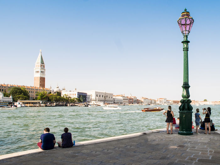 People on promenade by venetian lagoon against clear sky