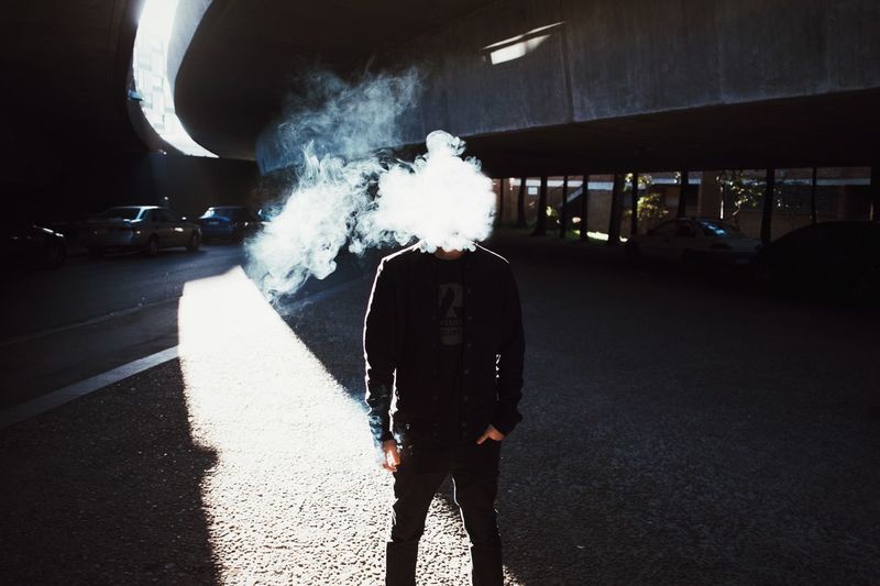 Man face covered with smoke standing below bridge