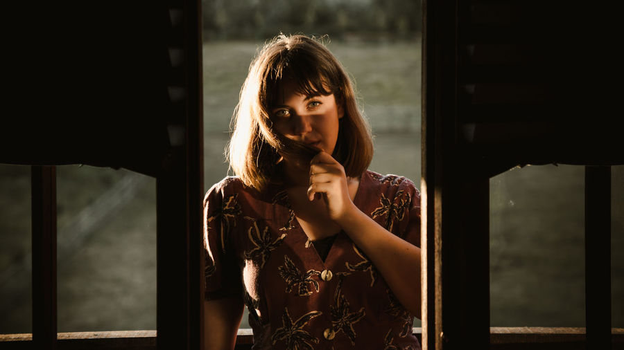 Portrait of a young woman on ledge of wooden cabin at sunset