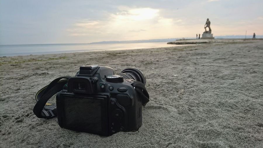 Close-up of camera at sandy beach against sky during sunset