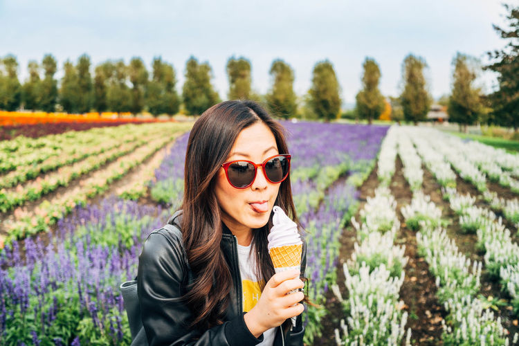 Young woman eating ice cream while standing against field