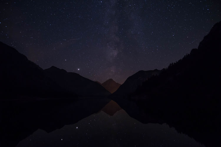Scenic view of lake and mountains against sky at night