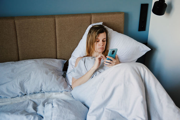 Woman using smartphone in the bed, social media, lazy weekend