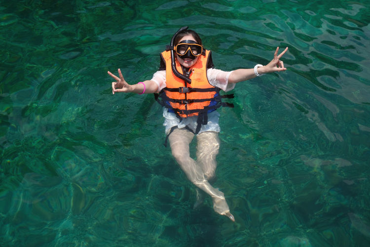 Portrait of smiling young woman showing peace sign while swimming in sea