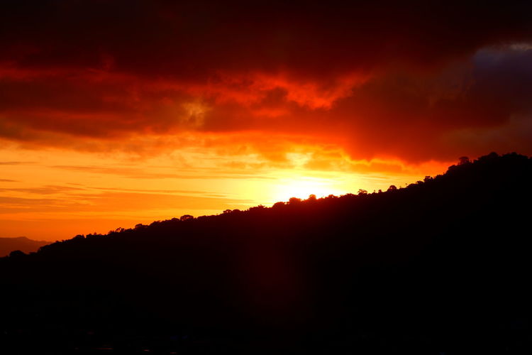 Silhouette landscape against dramatic sky during sunset
