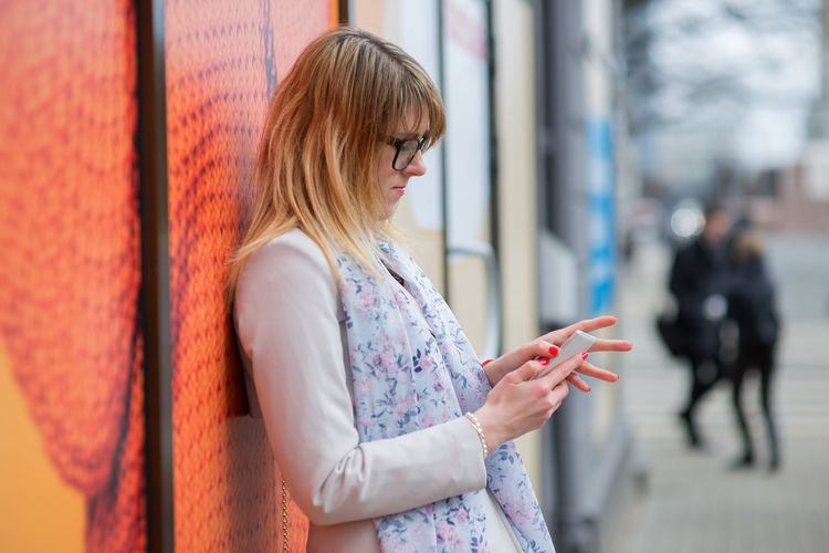 Side view of young woman using mobile phone while leaning on wall
