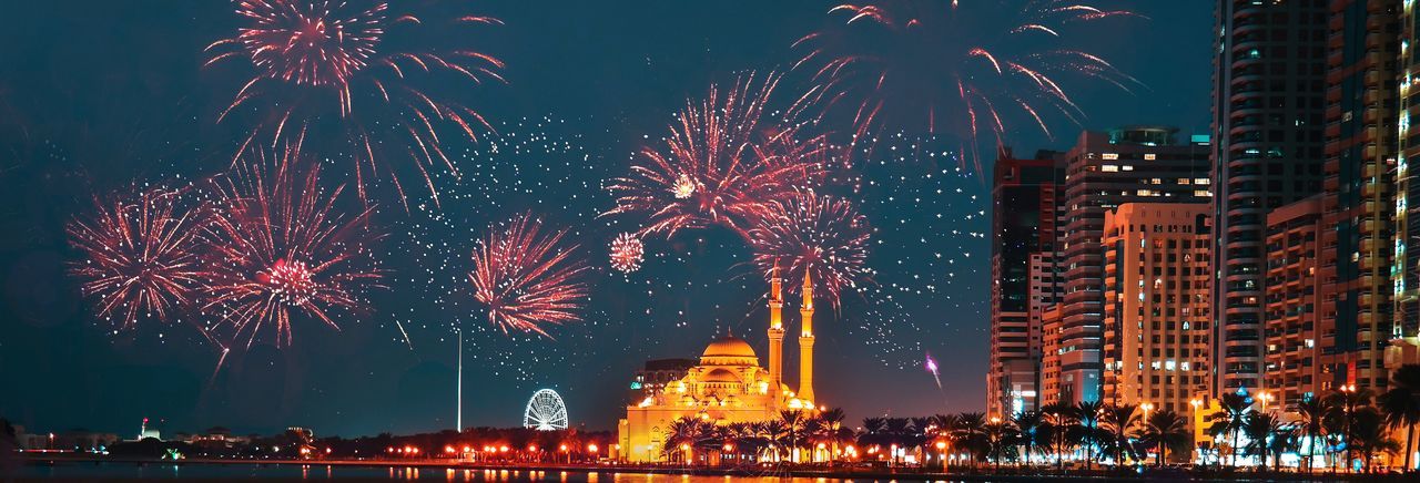 Firework display behind mosque in city against sky at night