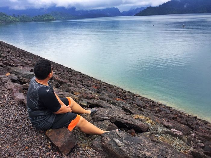 Man sitting on rock while looking at lake