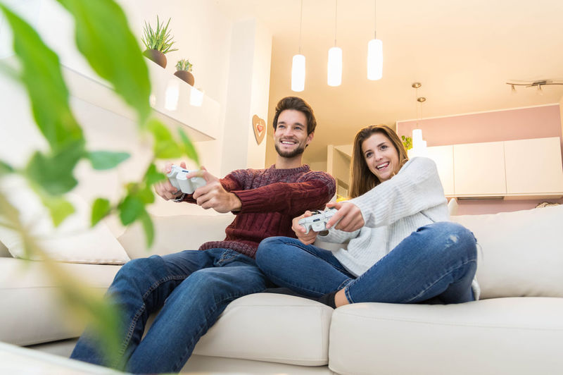 Low angle view of happy young couple playing video game while sitting on sofa at home