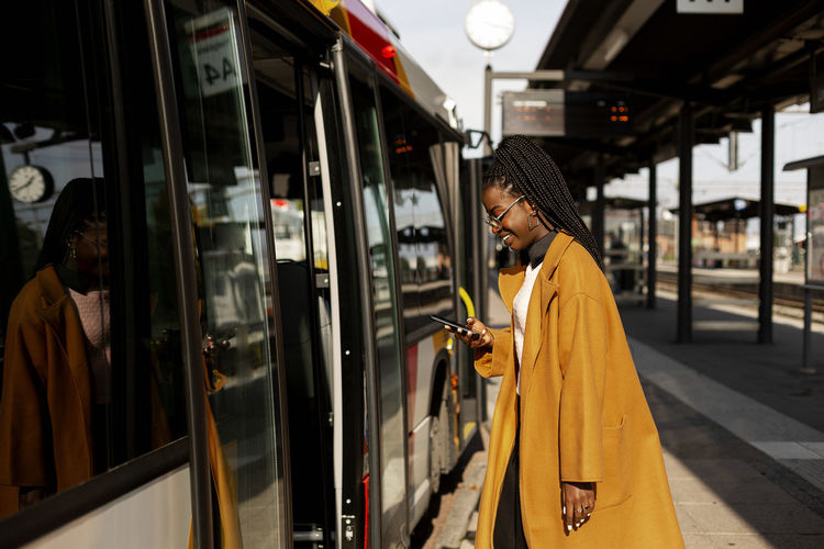 Smiling woman using phone while entering bus