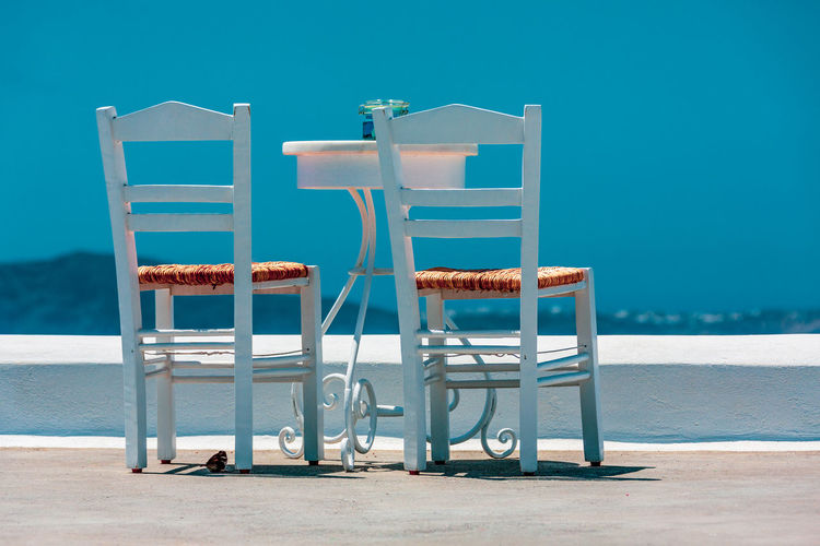 Two chairs and a table on white terrace, santorini greece.