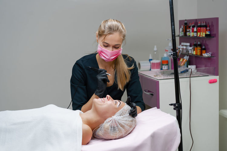 Cosmetologist wearing mask treating woman at clinic