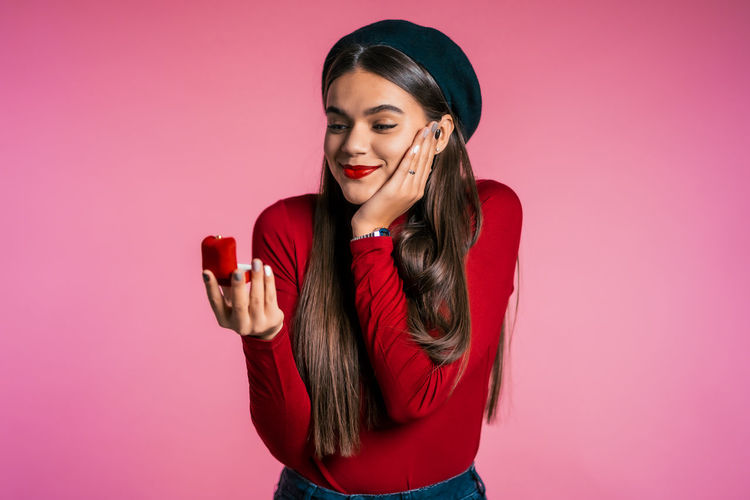 Smiling young woman using phone while standing against pink background