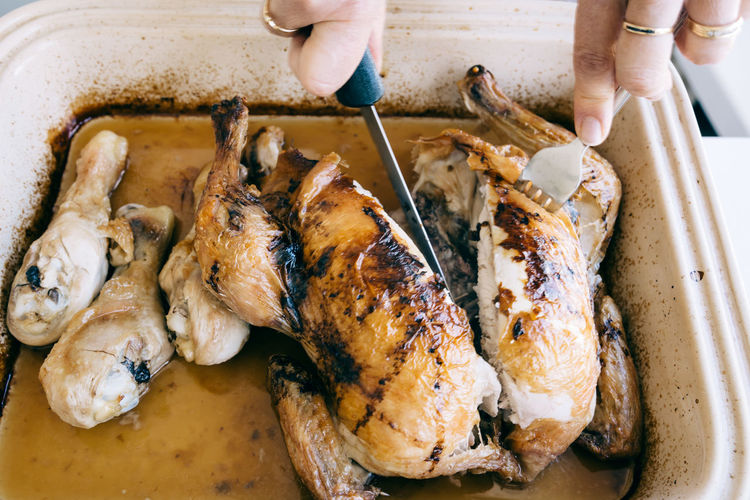 Cropped hands cutting roast chicken in container