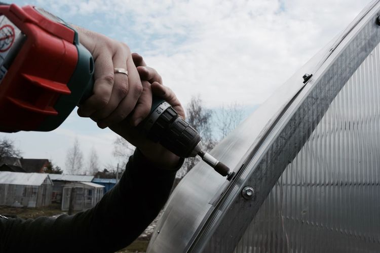 Cropped hands drilling in metal against sky
