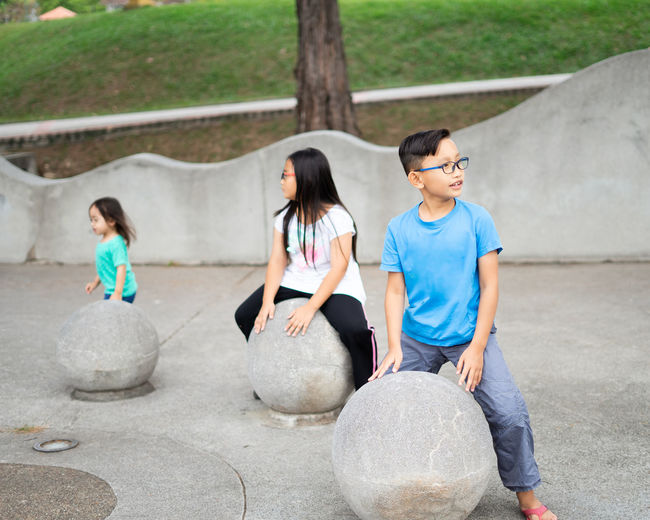 Asian children sitting on the concrete sphere ball shape in the park.