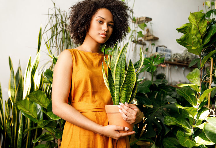 PORTRAIT OF WOMAN STANDING BY PLANTS