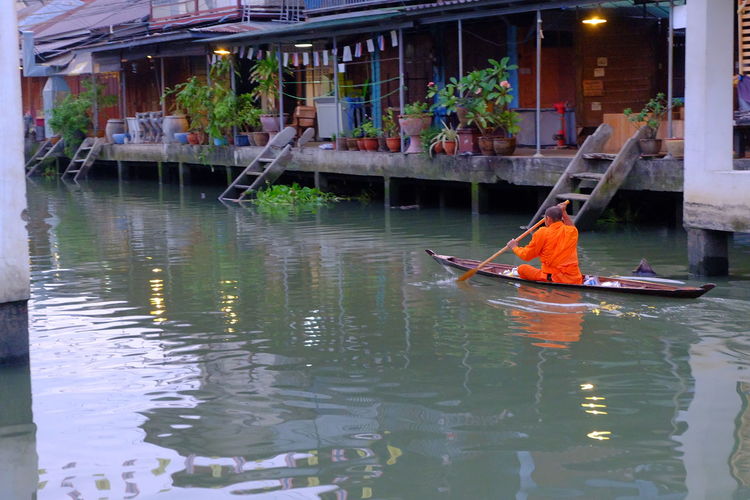 Rear view of monk boating on canal at floating market in city