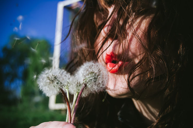 Close-up of woman blowing dandelions on sunny day