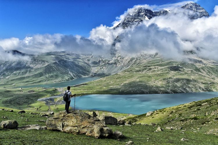 Man standing on a rock enjoying thescenic view of fresh water lake with mountains in the backdrop