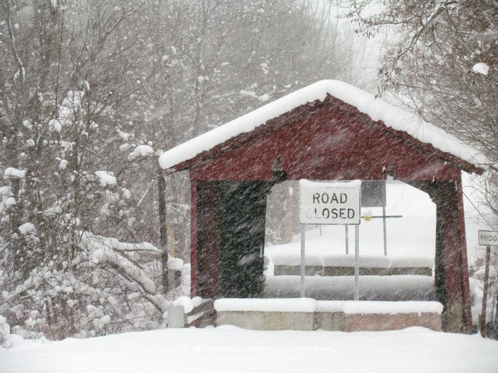 Road closed sign on built structure in snowy weather