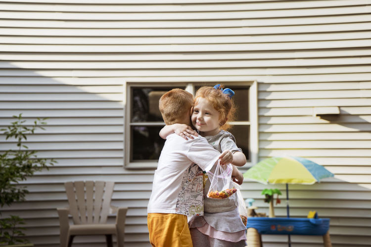 Cute children embracing while holding chocolate bags against house