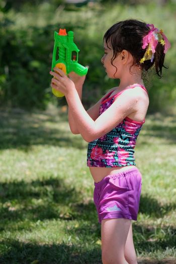 Side view of girl holding squirt gun in yard