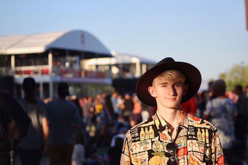 Portrait of young man wearing hat while standing in city against clear sky