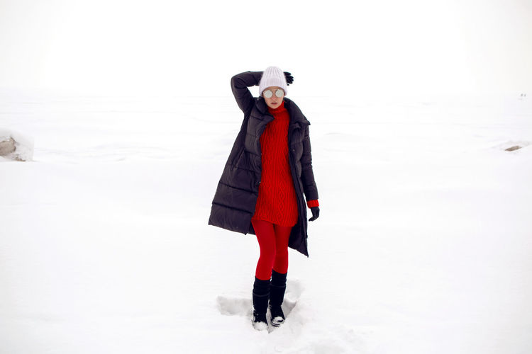 Woman stands in a snowy field in a jacket and sunglasses